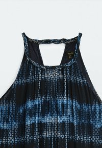 Käppärittä dress kevyessä kankaassa, jossa on merensininen ja sininen geometrinen kuvio; siinä on punottu halterneck ja löysä, hulmuava muoto.