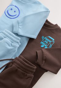 Two folded children's outfits, one light blue with a raised smiley face, one brown with a blue cartoon chocolate milk carton.