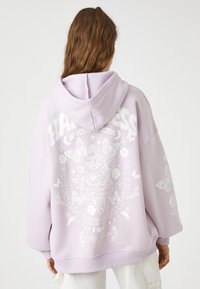 Przesadny hoodie w jasnym lawendowym kolorze, z białymi nadrukami kwiatowymi i motylkami. Zawiera kaptur ze sznurkiem i ściągacze na rękawach.