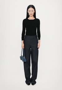 Black long-sleeve top, dark blue high-waisted jeans, and a small blue handbag made of denim. Model stands against a plain white background.