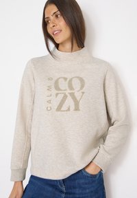 Světle béžová mikina s vysokým límcem, zdobená texturovanou výšivkou "CALM & COZY" ve zlaté barvě. Měkká tkanina s volným střihem a žebrovanými manžetami.