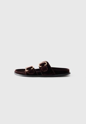 Sandale glissière en velours brun foncé avec deux boucles en or ajustables et une semelle noire plate sur fond blanc.