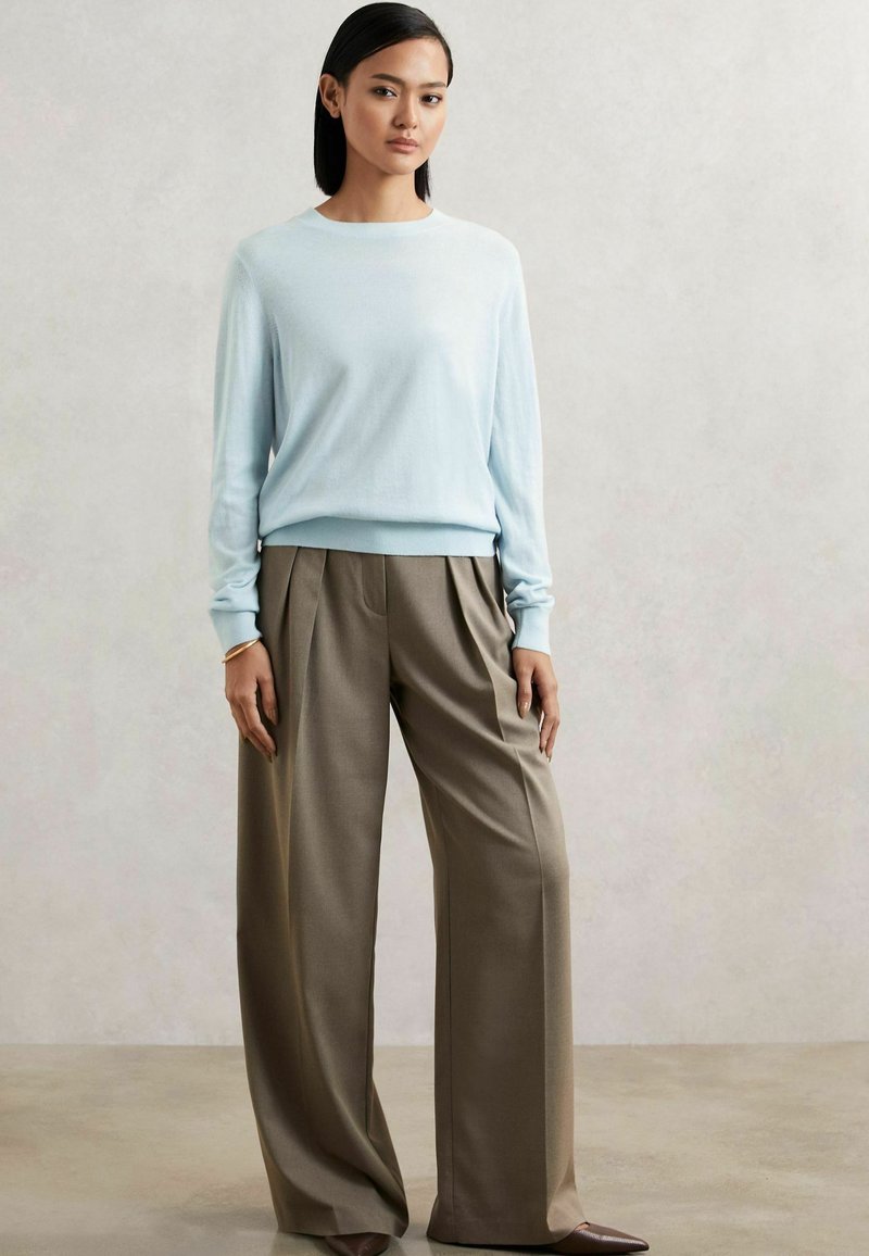 Hellblauer, langärmeliger Pullover mit rundem Halsausschnitt, kombiniert mit hochgeschnittenen, weiten braunen Hosen, die einen lockeren Sitz kreieren.