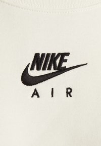 Tissu blanc avec le logo "NIKE AIR" brodé en noir, présentant un design emblématique de swoosh. Texture lisse, style minimaliste.