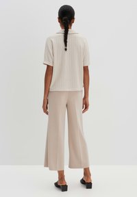 Hellbeige, gerippter Kurzarmoberteil kombiniert mit beigen, weit geschnittenen Hosen. Schwarze, offene Schuhe runden das Outfit ab. Glatter, lockerer Schnitt.