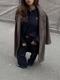 Tumši pelēks garš mētelis pār tumši zilā džempera ar rakstu, kombinēts ar platajiem tumšajiem džinsiem un ziliem augstpapēžu apaviem ar noapaļotu purngalu.