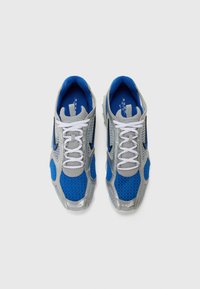 Baskets de sport bleu et gris avec un dessus en mesh, une semelle rembourrée et des lacets blancs. Des accents métalliques et un design épuré sont à noter.