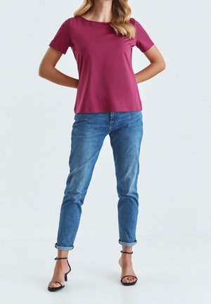 Fuksjowy top z krótkim rękawem i okrągłym dekoltem, w połączeniu z niebieskimi jeansami z podwiniętymi nogawkami oraz czarnymi sandałami na obcasie. Gładka faktura materiału.