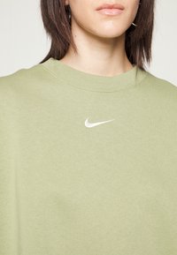 Světlé zelené mikina vyrobená z měkké tkaniny, s kulatým výstřihem a malým bílým logem Nike na hrudi. Hladká textura.