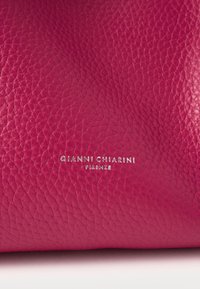 Cyklamenowa skóra o fakturowanej powierzchni, z wyraźnym srebrnym tłoczonym napisem "GIANNI CHIARINI FIRENZE".
