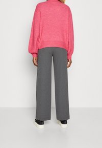 Un pull surdimensionné rose avec des manches ballon, associé à un pantalon large gris et des baskets noires. Le matériau semble doux et texturé.