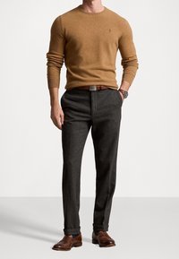 Brun tröja i stickat material, ihop med mörkgrå skräddarsydda byxor. Bruna läderskor fulländar outfiten. Polo-logotyp på tröjan.