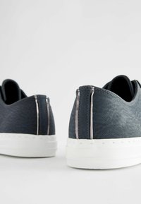 Baskets en tissu bleu avec un motif texturé, semelle blanche et accents argent métallisé au niveau du talon et des coutures latérales. Design à bout arrondi.