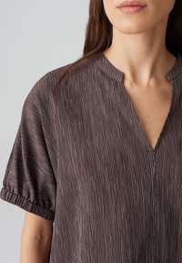 Blusa marrone scuro con texture a righe verticali, maniche a sbuffo corte e scollatura a V, con delicate rifiniture elastiche ai polsini delle maniche.