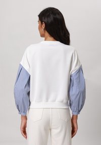 Vit sweatshirt med puffärm i blått och vitt randigt mönster. Slät tyg med ribbad kant vid ärmslut och midja. Avslappnad passform och design.