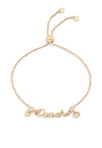 Bracelet ton or avec un pendentif "Coach" en écriture cursive, un cœur décoratif et deux accents en cristal sur une fine chaîne à fermeture réglable.