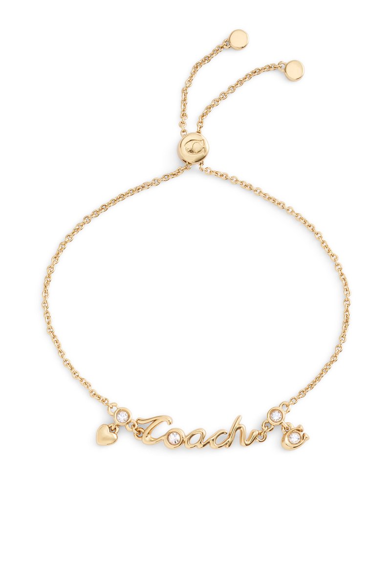 Bracelet ton or avec un pendentif "Coach" en écriture cursive, un cœur décoratif et deux accents en cristal sur une fine chaîne à fermeture réglable.