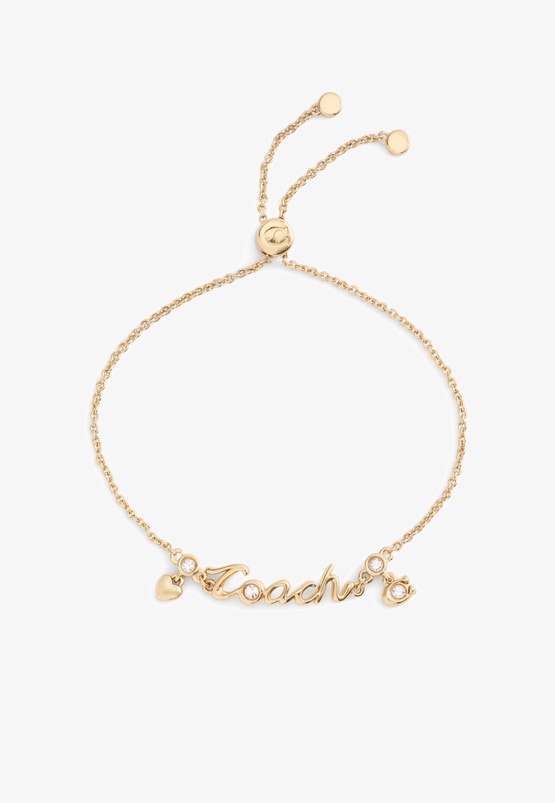 Bracelet ton or avec un pendentif "Coach" en écriture cursive, un cœur décoratif et deux accents en cristal sur une fine chaîne à fermeture réglable.