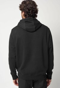 Sudadera negra de tela suave, con capucha, puños y cinturilla de canalé. Diseño liso sin patrones ni adornos.