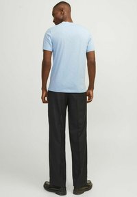 Camisa de manga corta azul clara en un tejido suave y texturizado, combinada con pantalones formales oscuros y calzado negro. Vista desde la parte trasera.