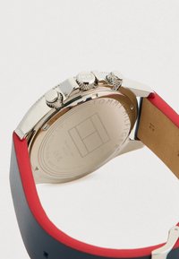 Retro della cassa di un orologio da polso in acciaio inossidabile argentato con tre pulsanti e un bracciale in pelle rossa e blu.