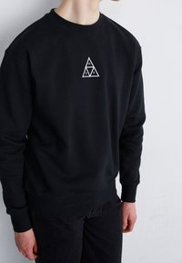Black sweatshirt with ribbed cuffs and hem, featuring a white triangular logo on the chest. Soft texture, casual fit.