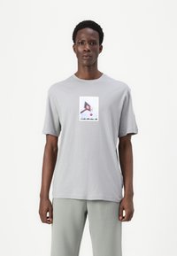 Grå bomulds T-shirt med korte ærmer, med et centralt grafisk motiv af en basketballkurv og bold på en hvid rektangulær baggrund.