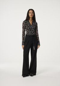 Zwarte doorzichtige blouse met witte handgeschreven tekst, gecombineerd met zwart high-waisted wijde broek met een decoratieve accenten.