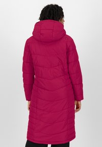 Frau in einem langen, gepolsterten, magentafarbenen Wintermantel mit Kapuze, von hinten vor einem einfarbigen Hintergrund gesehen.