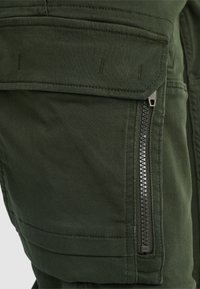 Donkergroene cargobroek met een ritssluiting aan de zijkant, versterkte stiksels en een gestructureerde stofafwerking. Praktisch ontwerp voor gebruiksgemak.