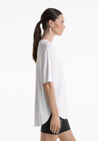 Haut blanc à manches courtes avec une coupe décontractée, texture lisse, encolure arrondie et ourlet asymétrique, associé à un short noir.