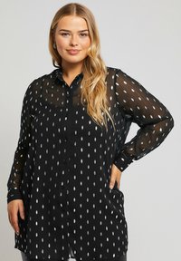 Zwarte blouse met lange doorschijnende mouwen, gepunte zilveren bladvormen, knopen aan de voorkant en een losse pasvorm. Zachte stof met een lichte glans.