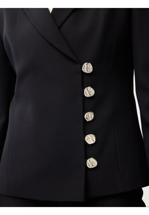 Sort tætsiddende blazer med fem uregelmæssige, teksturerede sølvknapper, arrangeret vertikalt på højre forside.
