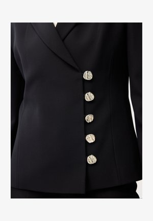 Černé přiléhavé sako s pěti nepravidelnými stříbrnými knoflíky s texturou, uspořádanými vertikálně na pravé přední straně.