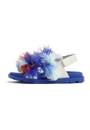 Blå och vita sandaler med fluffiga pom-poms i flerfärgade nyanser av blått och rött på remmen. Texturerad blå sula med kardborrestängning.
