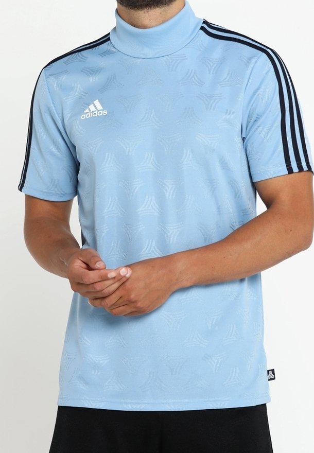 Ljusblå Adidas t-shirt med kort ärm och svarta axelränder samt subtilt mönstrad textur, bärs av person med hopknäppta händer.