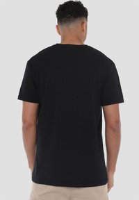 Black cotton t-shirt with short sleeves and a crew neckline. Smooth texture, simple design, no visible logos or patterns on the back.