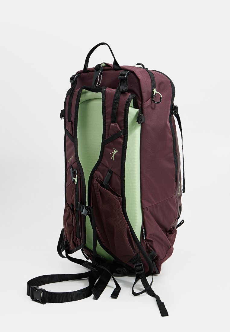 Mochila color burdeos con acentos negros; cuenta con un interior verde, múltiples bolsillos, correas y cremalleras. Tela duradera con respaldo acolchado.