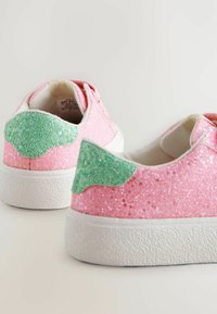 Glittriga rosa sneakers med gröna texturerade detaljer på hälen, med en vit gummisula och rundad design.