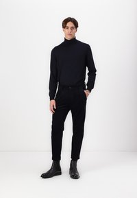 Black turtleneck sweater, fitted design, paired with black slim-fit pants. Outfit complemented by shiny black ankle boots.