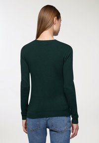 Zielony sweter dzianinowy z długimi rękawami i okrągłym dekoltem, z ribbowym wykończeniem u dołu i na mankietach, w połączeniu z jasnoniebieskimi dżinsami.