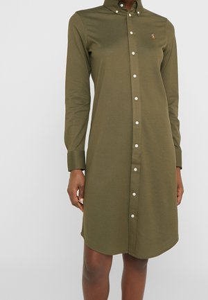 Oliwkowa sukienka na guziki z kołnierzykiem, długimi rękawami i białymi guzikami. Na piersi znajduje się logo. Wykonana z mieszanki bawełny.