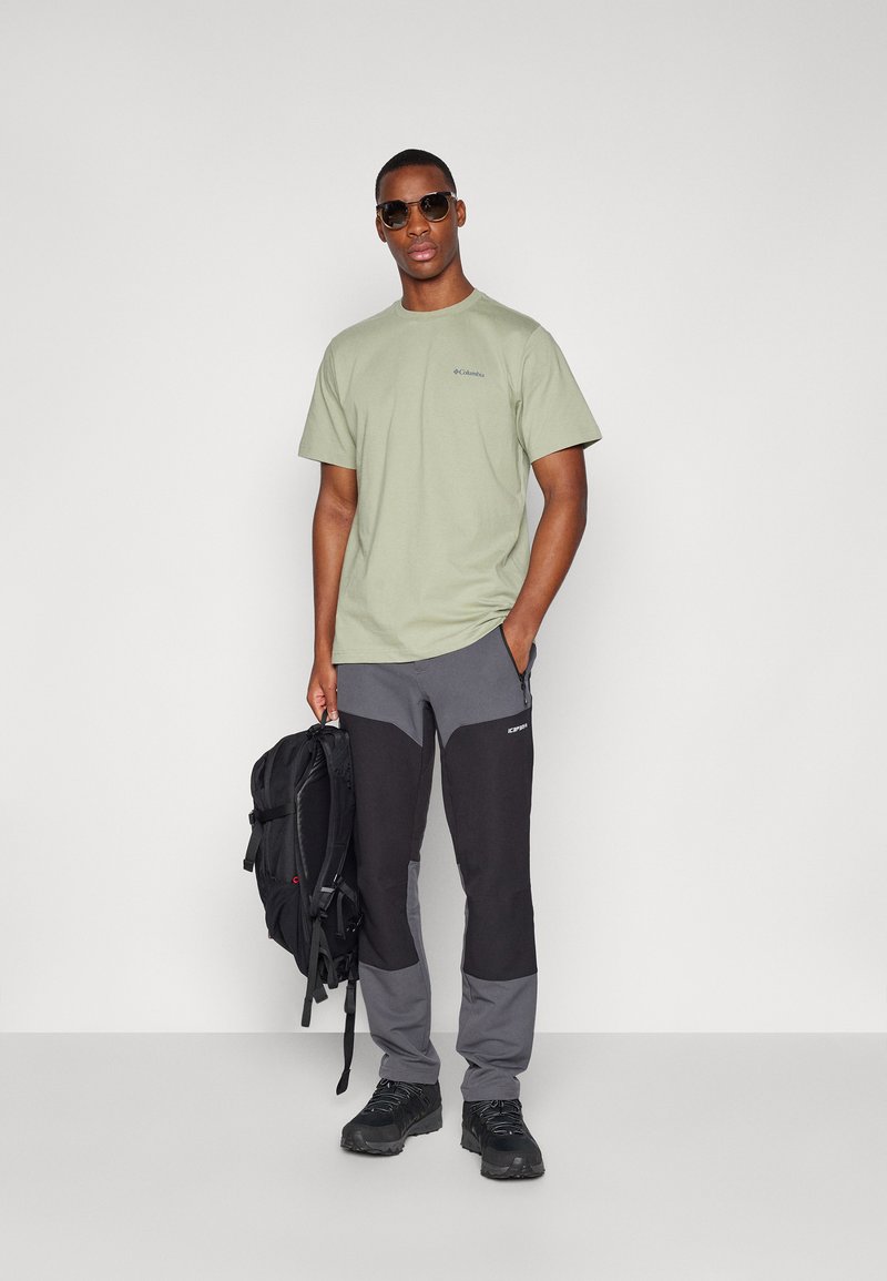 Jasnozielona bawełniana koszulka z krótkim rękawem i logo. Ciemnoszare i czarne spodnie z zamkami. Czarny plecak i buty.