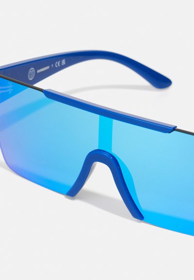 Blaue Sonnenbrille mit großen, umschließenden Gläsern und dicken Bügeln. Die Gläser haben einen Verlauf in Blau, und die Bügel sind glänzend.