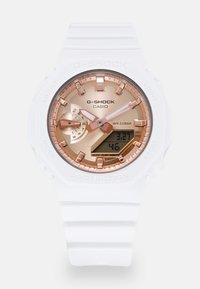 Montre G-SHOCK de Casio avec un bracelet en résine blanche, un cadran rose doré avec un affichage analogique-numérique, et une résistance à l'eau allant jusqu'à 200 mètres.