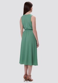 Rosa es un drapeado elegante de un solo hombro, diseñado con un corte asimétrico y adornos sutiles, complementado con unos pendientes dorados.