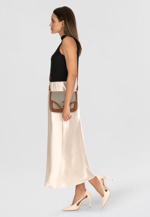 Top smanicato nero a coste, gonna maxi in satin color crema, scarpe con tacco beige e una borsa a tracolla grigia con accenti marroni e hardware dorato.