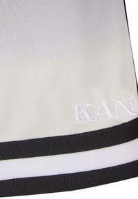 Tissu blanc texturé avec bordure rayée noire et blanche en bas et broderie blanche en relief "KAN" partiellement visible.