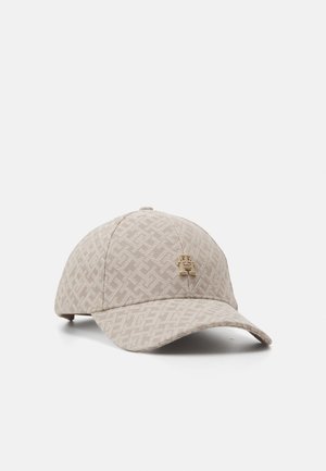 Beige baseballpet met een gestructureerd geometrisch patroon en een klein gouden embleem aan de voorkant, afgebeeld tegen een eenvoudige lichte achtergrond.