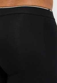 Schwarze Sportshorts mit glatter Textur und eng anliegendem Design. Der Bund hat kontrastierende Nähte und Logo-Details.